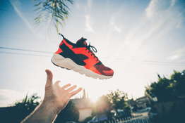 A hand throws a shoe into the air against the backdrop of a sunrise