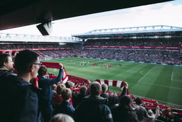 Liverpool fans carrying banners cheer the start of a soccer game at Anfield stadium.