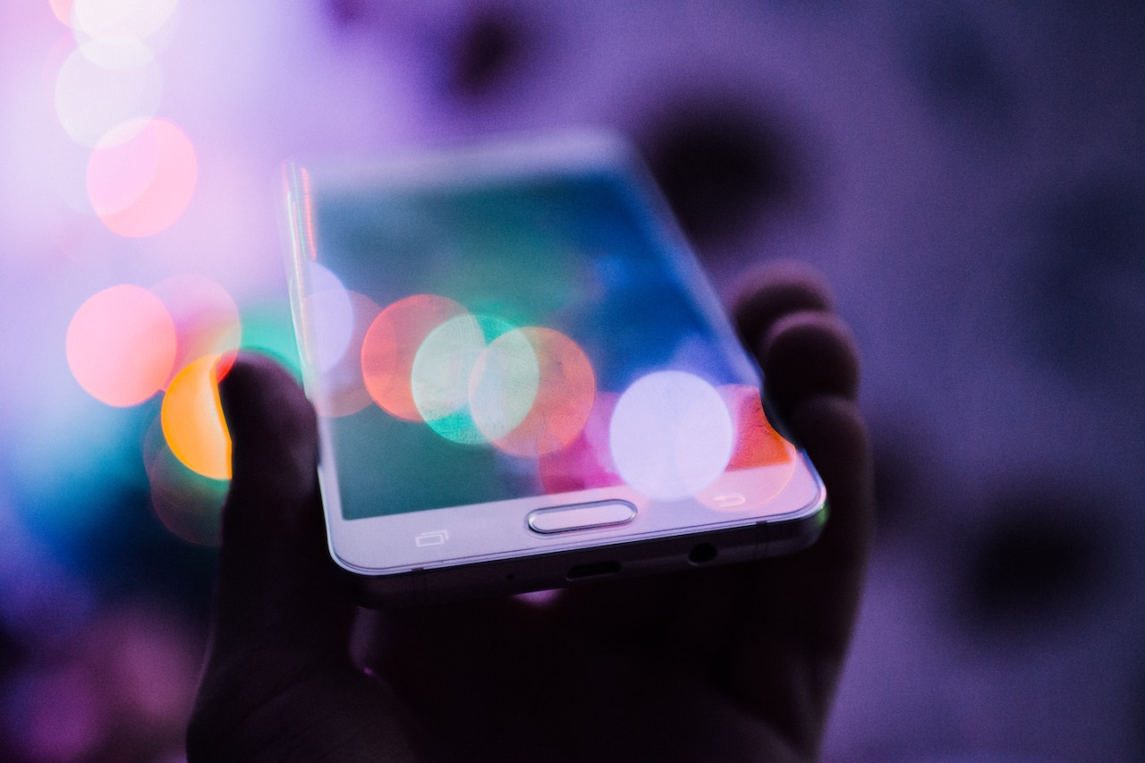 Your customer’s hand holding a cell phone with pastel bokeh surrounding it, just as your customer abounds with joy when immersed in a phygital experience