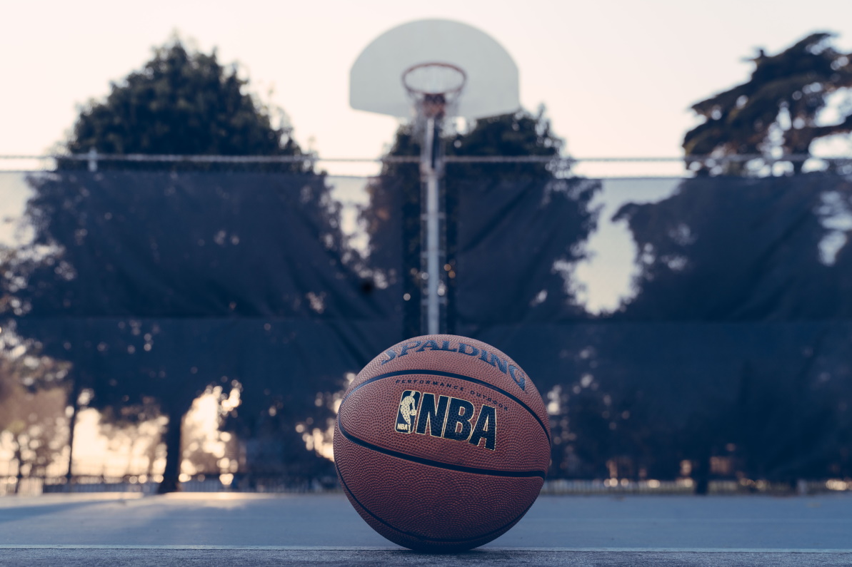 An officially licensed basketball rests on an outdoor court with the basket in the background